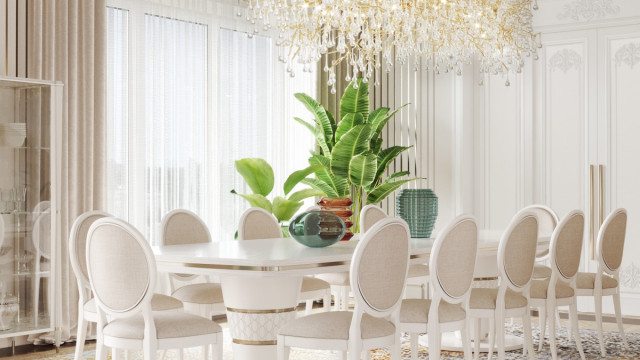 This picture is a photo of a luxurious modern living room designed by Antonovich Design. The room features a white marble floor with a cream-colored rug, a white sofa, two armchairs with gold accents, a round table with a glass top, and a black leather ottoman with gold trim. The walls are painted a soft grey shade and adorn several pieces of wall art. The room also features a wooden ceiling with recessed lighting and a large built-in fireplace with a marble mantel.