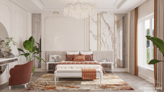 This picture shows a luxurious, modern living room designed with marble and warm beige tones. It features a large white leather sofa with decorative pillows and ornate brass accents. The walls are finished with elegant marble tiling and a modern LED chandelier hangs from the ceiling. A round glass coffee table and two white armchairs complete the look.