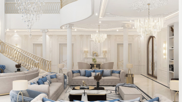 This picture is of a luxurious living room designed by Antonovich Design. The room features a classic and modern aesthetic, with golden accents and a grand symmetrical layout. There are two large cream-colored sofas facing one another, with a glass coffee table between them. On either side of the sofas are two matching armchairs, along with a round end table. A pale grey rug covers the floor, and a tall marble fireplace is visible in the background. The walls are a deep navy blue, with a large golden mirror above the fireplace for added elegance.