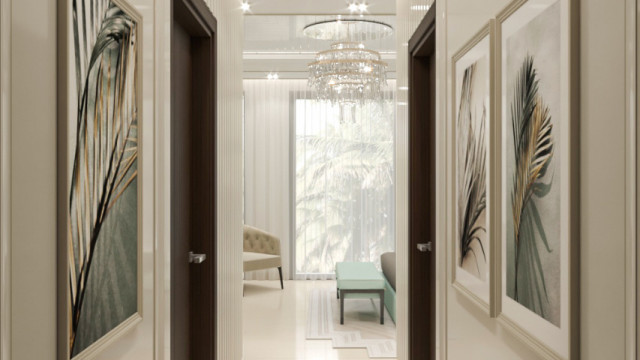 This picture shows a stunning hallway in a luxury home. This hallway has an intricate ceiling design with ornate chandeliers, marble stairs leading up to a balcony, and a large round table with two gold chairs that are placed opposite the stairwell. The walls are painted in a warm cream color and decorated with stylish artwork, adding to the luxurious look of the room.