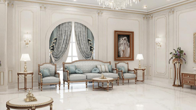 This picture shows a luxurious living room interior design from Antonovich Design. It features plush cream colored furniture, including a large sectional sofa, a round ottoman, and two armchairs. The walls are painted in a deep blue tone, while silver and gold accents add a hint of shimmer, creating an overall elegant and inviting atmosphere. The floors are covered in an intricate light-colored rug, with ornate details on the walls and ceiling adding to the luxurious effect.