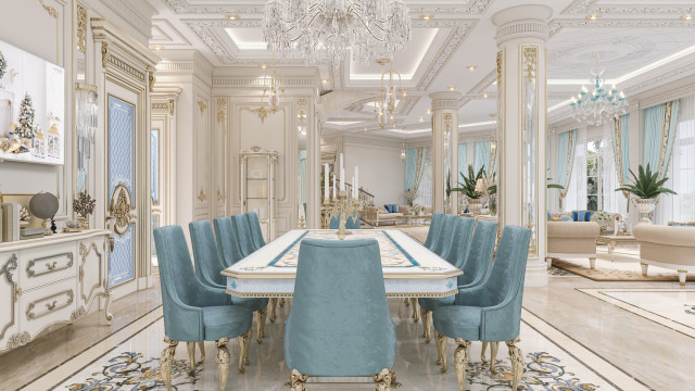 This picture shows an ornately decorated dining room in an upscale home. The walls are painted a pale gray, and the ceiling is adorned with intricate crown molding. An elegant chandelier hangs from the center of the room, illuminated by wall sconces on either side of the room. A large wooden dining table is surrounded by plush chairs upholstered in a light beige fabric. A vase of flowers adds a splash of color to the room, while an ornate sofa provides an inviting spot to relax.