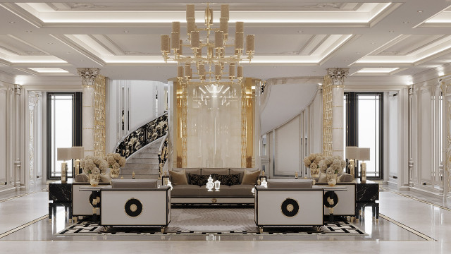 This picture shows a luxurious, modern living space. The room has a custom designed marble floor with a grand chandelier hanging from the ceiling. The walls are painted white and feature art on each side. There are several crystal-encrusted furniture pieces, including a light brown leather sofa with two accent chairs, a glass coffee table, and a round ottoman. Several pieces of art hang from the walls, including a large framed oil painting.