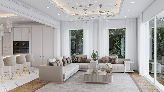 This image shows a luxurious modern living room designed by Antonovich Design. The room features a U-shaped light-colored sofa upholstered in grey with several patterned velvet pillows and a light wooden coffee table. There are matching side tables, and a tall lamp that creates a warm glow. The walls are painted a light blue and have an abstract art piece on the wall. There is also a large mirror that reflects the cozy atmosphere.