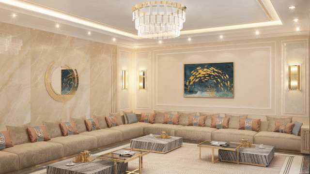 This picture shows a modern and luxurious bedroom area. The walls and ceiling are done in a pale gray color and feature two large, crystal chandeliers hanging from the center of the room. The walls are also adorned with multiple gold accents and detailed trim. The bed is an elegant four-poster style featuring silky ivory bedding and a number of decorative pillows. On either side of the bed are two matching night stands with glass tops, and in the corner is an upholstered chair. The flooring is done in a rich hardwood that adds to the sophisticated atmosphere