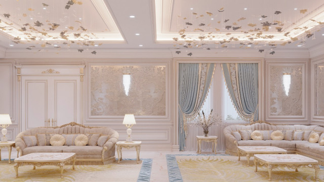 The picture shows the interior of a modern and luxurious living room. It features an extravagant off-white couch that is accented with gold details. There are two round end tables with tall glass lamps in the middle. The wall behind the couch is adorned with framed art pieces, and there is a bold colorful rug beneath the seating area. On either side of the couch are two matching armchairs, and the floor is finished with a patterned rug.