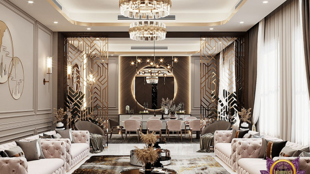 This picture shows a luxurious, modern interior design with beige upholstered furniture and a ornate wooden coffee table. The walls are painted white and the floor is dark marble with a geometric patterned rug. The ceiling also has a white marble finish and there is a large chandelier hanging from it. There is a round window in the background with red curtains, and small plants in the corner of the room.