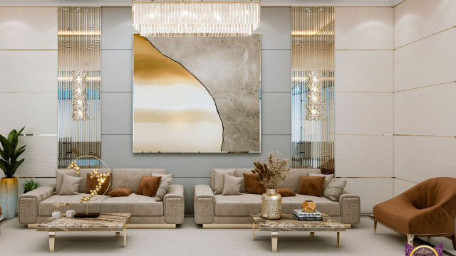 The picture shows an elegant, modern-style living room with luxurious furnishings. The room features a patterned wall with a high, arched ceiling and recessed lighting. There is a large cream velvet sofa facing a metal and glass coffee table, and two cream armchairs against the wall. The floor is tiled in grey stone, and there is a plush grey rug beneath the seating area. In the back corner of the room is a marble fireplace surround with inlaid wood accents.
