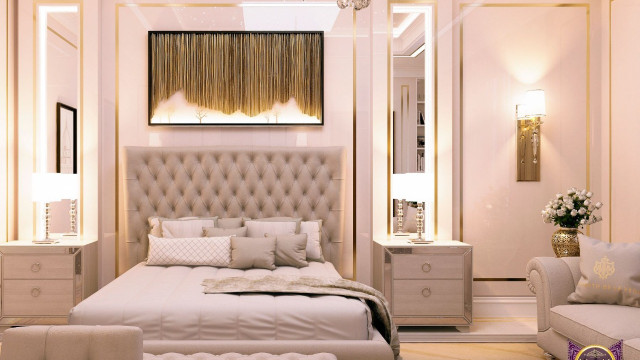 jpgThis picture shows an elegant contemporary bedroom design. It features a large, white leather bed with a sculptural headboard and tall white tufted nightstands adorned with gold lamps on either side. The walls are a light shade of blue and a large window provides natural light and a view of the outdoor scenery. A round white ottoman sits in the corner of the room and several modern abstract art pieces decorate the wall. The floor is covered in a plush area rug in shades of cream and pink, while a white upholstered bench sits at the foot of the