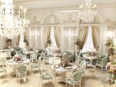 This picture is showing a luxurious dining room with classic, ornate furnishings and decor. The room features a long wooden dining table with carved detailing and a white marble tabletop. Around the table are elegant dining chairs upholstered in a soft fabric or velvet. There are two tall, floor to ceiling windows that provide ample natural light. The walls are painted a neutral shade with white trim and gold accents. A large crystal chandelier hangs from the ceiling and the flooring is a dark hardwood.