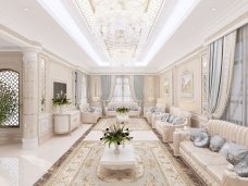 This picture shows a luxurious modern interior design. It features a curved sofa, a white fur rug, a gold pendant light, and an elegant crystal chandelier. The walls and the floors are adorned with patterned marble tiles, and the room is decorated with a botanical wallpaper. The walls also feature two gold mirrors and two wall-mounted shelves.