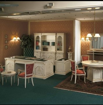 This picture displays an ornate, spacious living room. The room is decorated in classic style with a glossy white grand piano and comfortable seating furniture upholstered in cream velvet. There is an antique fireplace with a clock and two decorative vases on either side. The room is highlighted by an impressive wooden chandelier and a luxurious area rug. The wall-to-wall windows provide plenty of natural light, and the beautiful white crown molding completes the look.