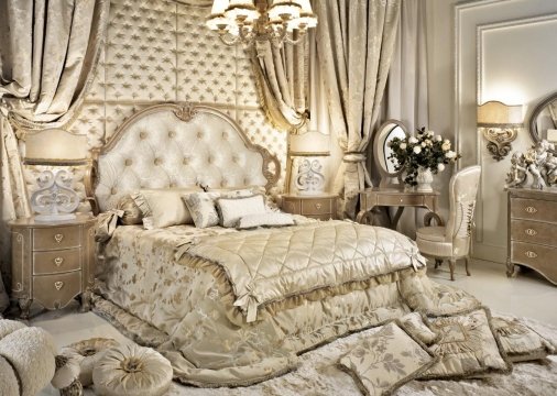 This is a luxurious bedroom designed by Antonovich Design located in the United Arab Emirates. The room features a large four-poster bed with an ornate headboard and footboard. Grey upholstered walls create texture and depth, while the gold accents throughout the room bring a touch of elegance to the design. The room has several luxurious light fixtures and is accented with a matching grey rug, making it look and feel like a royal suite.