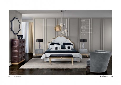 This picture shows a luxurious bedroom interior with a contemporary design. The bedroom features a large four-poster bed with white upholstery and a grey tufted headboard. On either side of the bed are two light wood nightstands with crystal lamps. The room is decorated with gold framed wall art above the bed, a large square mirror with an ornate white frame, and dark grey window curtains. The rest of the room is decorated in neutral tones with a light wooden floor.